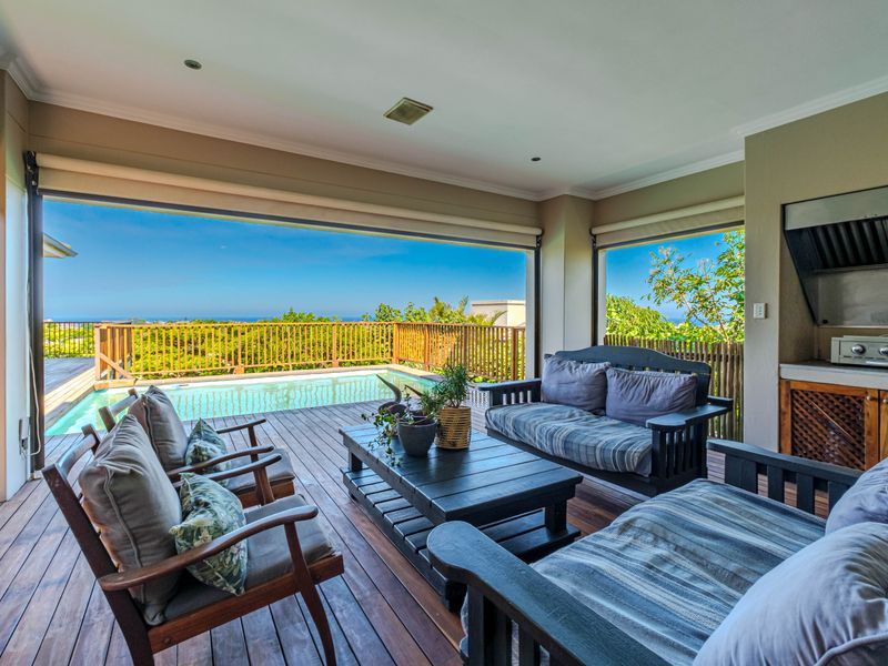 Covered outdoor patio featuring timber decking, a built-in braai area, and direct access to a swimming pool with scenic views.