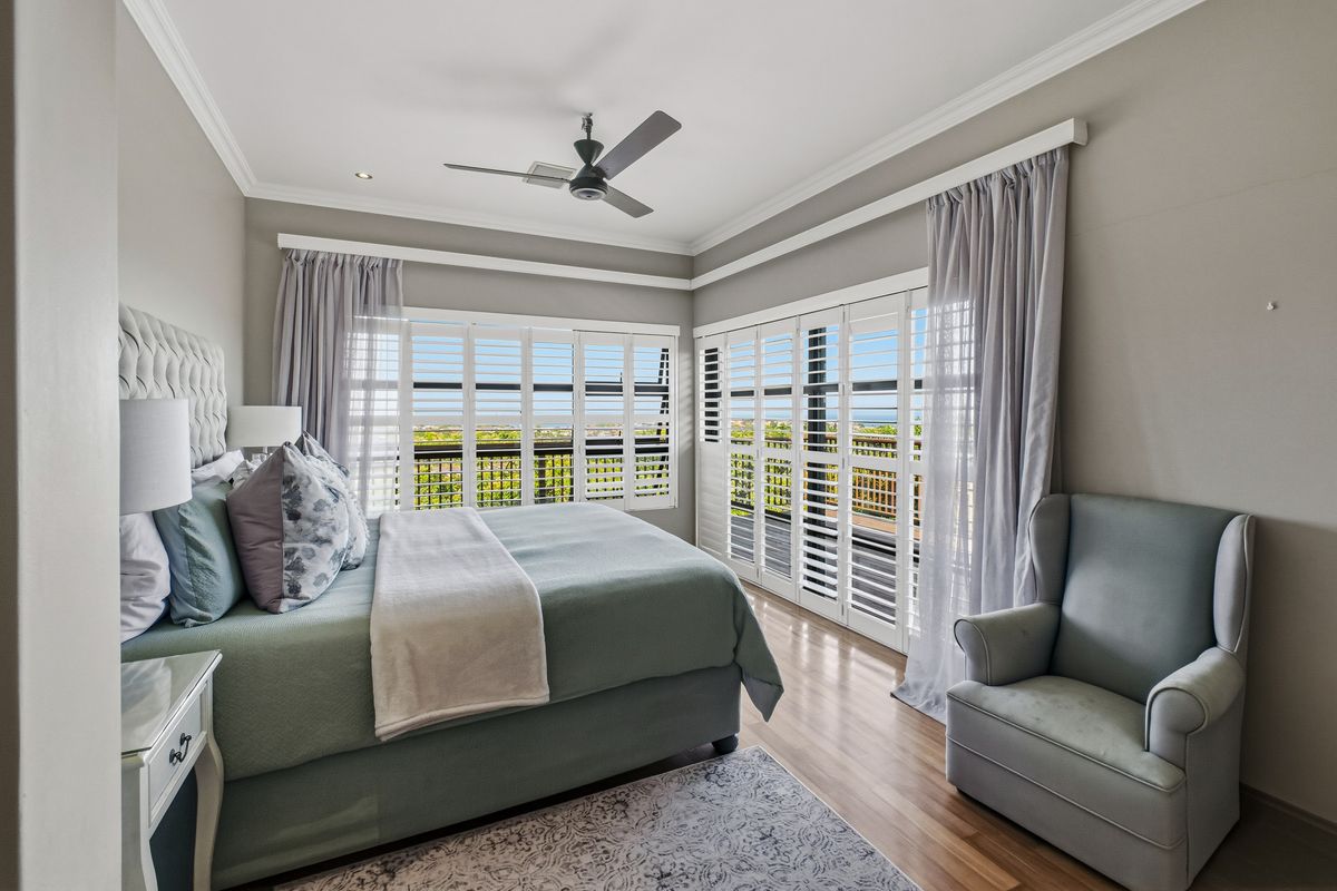 Spacious bedroom featuring hardwood flooring, crown molding, recessed lighting, and plantation shutters opening to a balcony with scenic views.