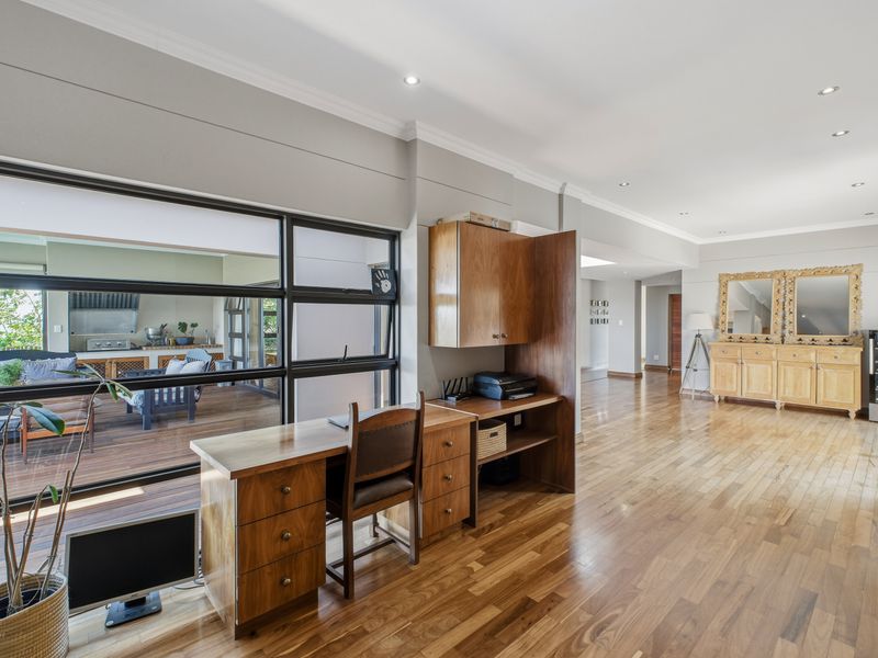 Spacious living area featuring polished hardwood flooring, recessed lighting, and large windows overlooking an outdoor deck, with integrated cabinetry and elegant crown molding.