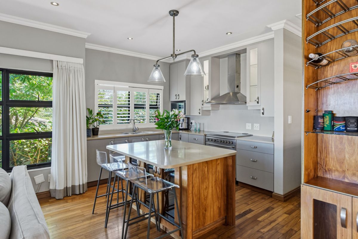 Modern kitchen featuring a central wooden island with stone countertop, stainless steel appliances, hardwood flooring, and elegant plantation shutters.