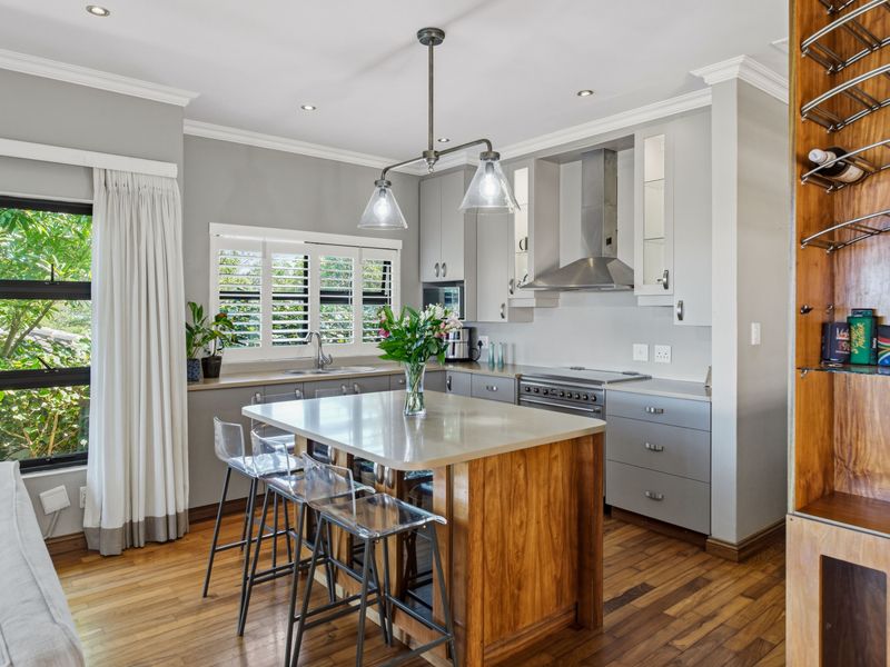 Modern kitchen featuring a central wooden island with stone countertop, stainless steel appliances, hardwood flooring, and elegant plantation shutters.