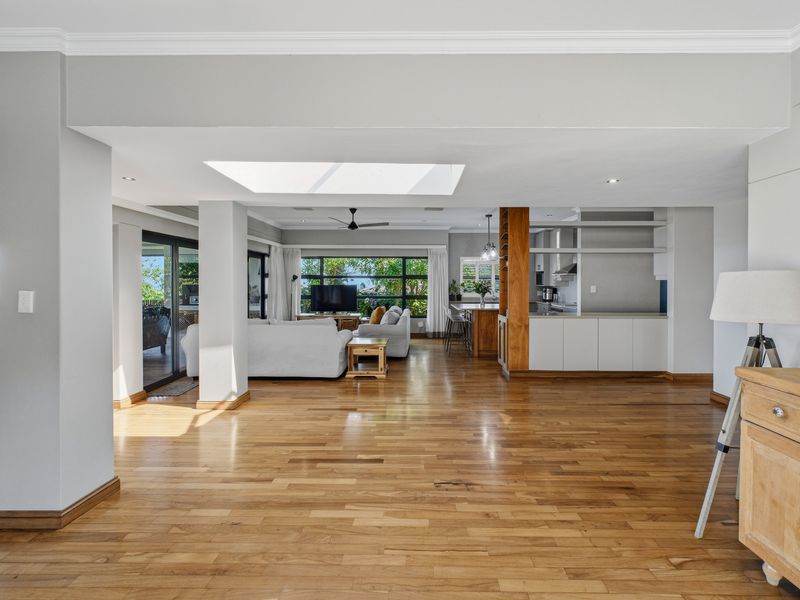 Spacious open-plan living and kitchen area featuring polished hardwood floors, a large skylight, and seamless flow to the outdoor patio through sliding glass doors.