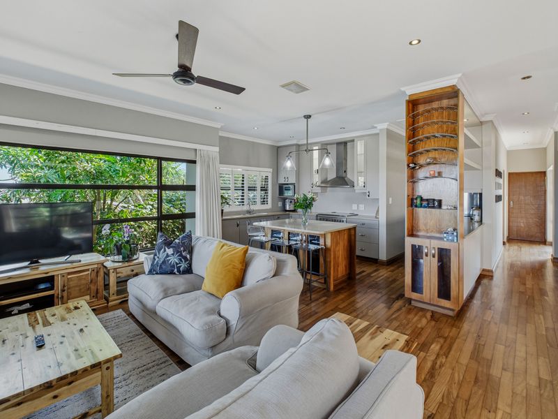 Spacious open-plan living and kitchen area featuring hardwood flooring, a central kitchen island, built-in wine storage, and large windows overlooking lush greenery.