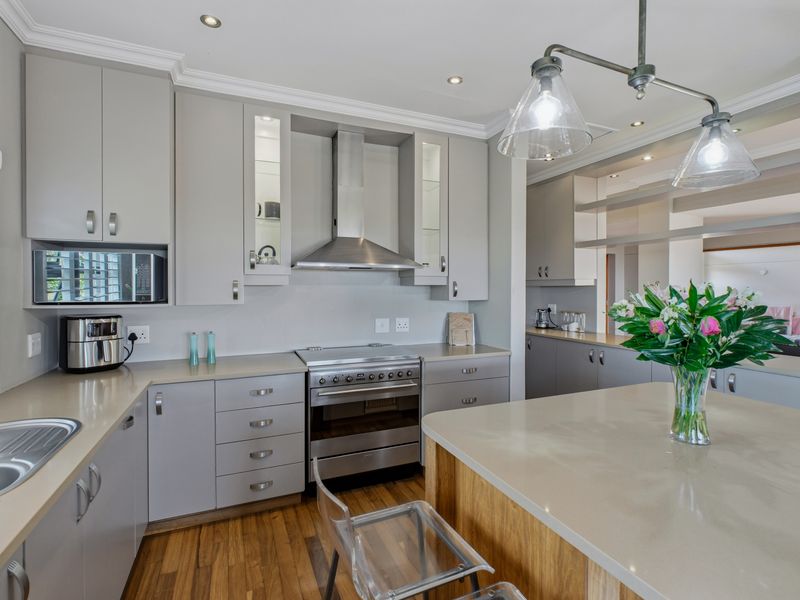 Modern kitchen featuring light grey cabinetry, stone countertops, a central island, stainless steel appliances, and hardwood flooring with recessed lighting.