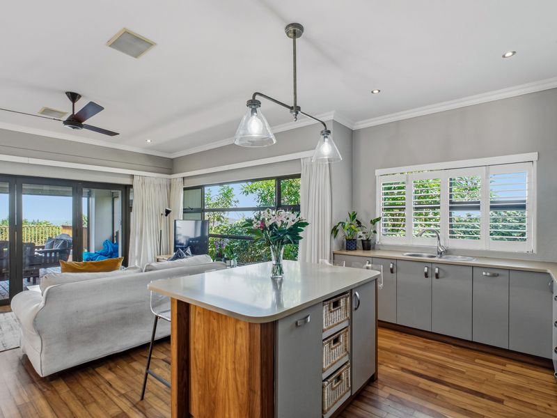 Modern open-plan kitchen and living area featuring a central island, quartz countertops, hardwood flooring, and seamless access to an outdoor patio through sliding doors.