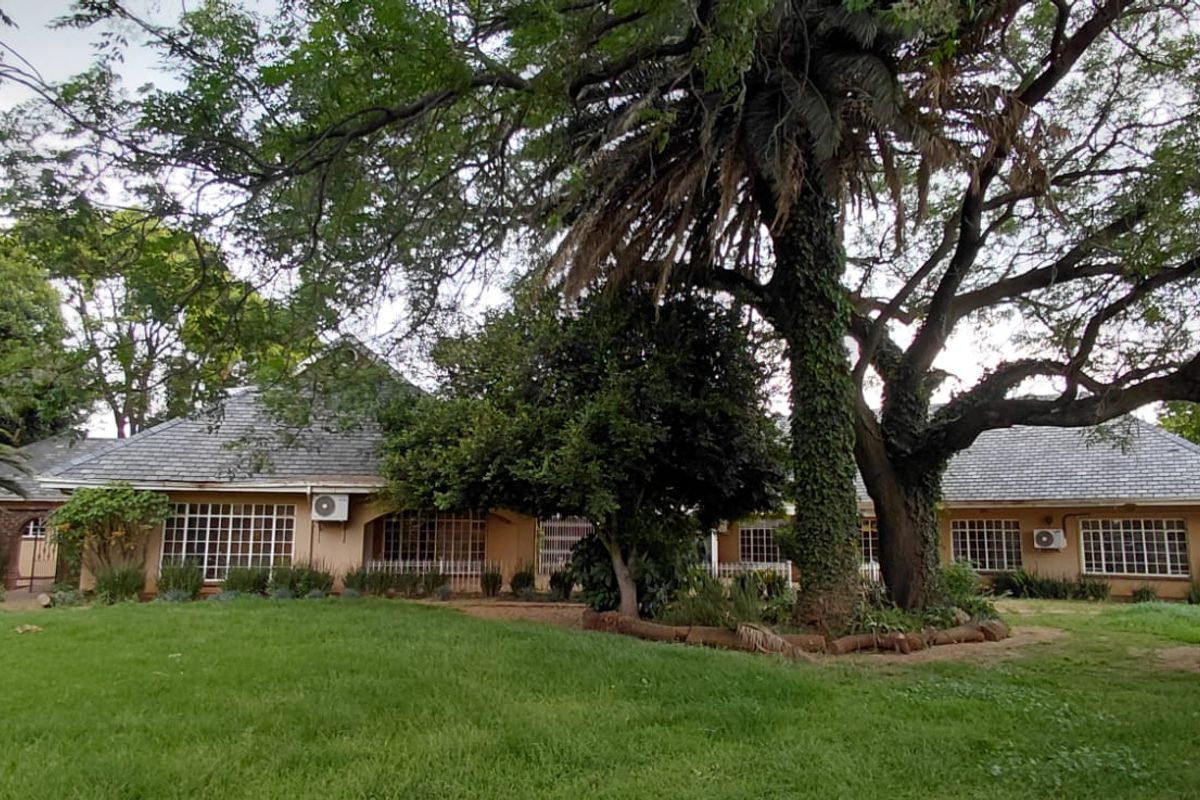 A view of the rear elevation of the house featuring a large, well-maintained garden with mature trees and grid-pattern windows.