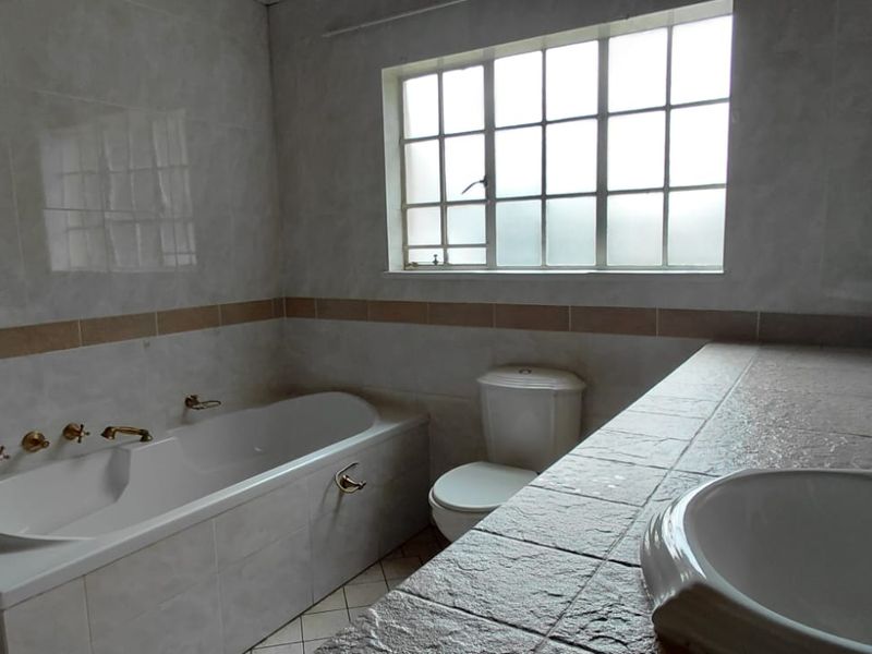 A functional bathroom featuring a built-in bathtub, toilet, and a tiled vanity area with a basin, offering a neutral base for renovation.