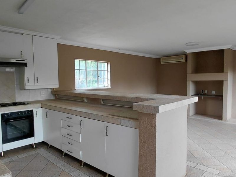 Spacious open-plan kitchen and living area featuring white cabinetry, tiled countertops, built-in oven, hob, and a cozy fireplace, offering a versatile layout.