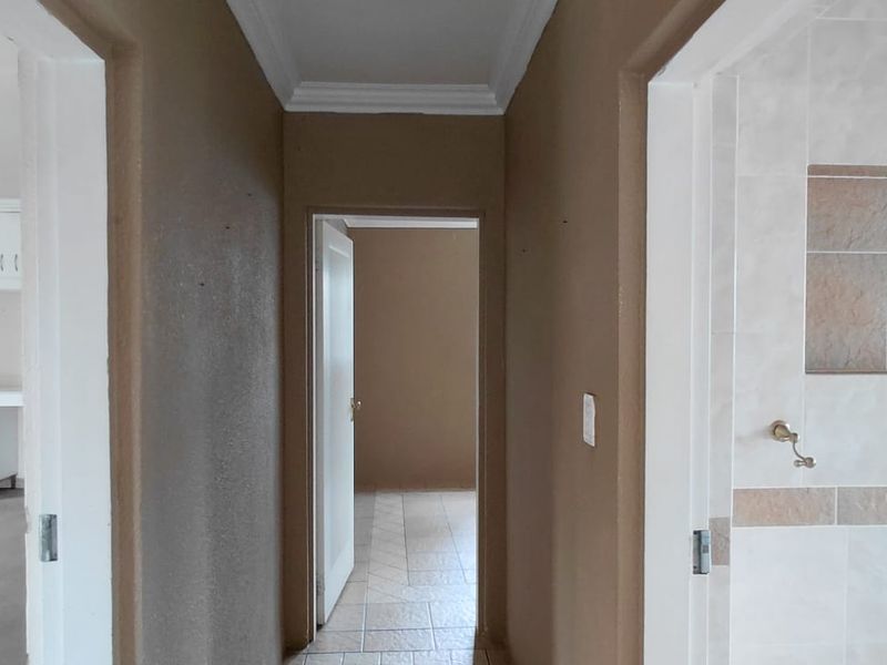A neutral-toned hallway connecting multiple rooms, featuring tiled flooring, crown molding, and access to adjacent living and bathroom spaces.