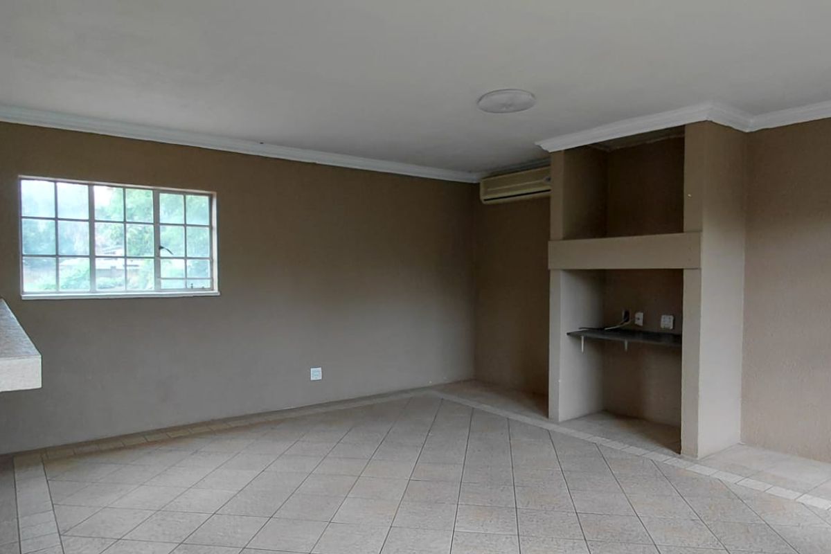 An empty living area featuring tiled flooring, a built-in shelving unit, a breakfast bar, and an air conditioning unit.