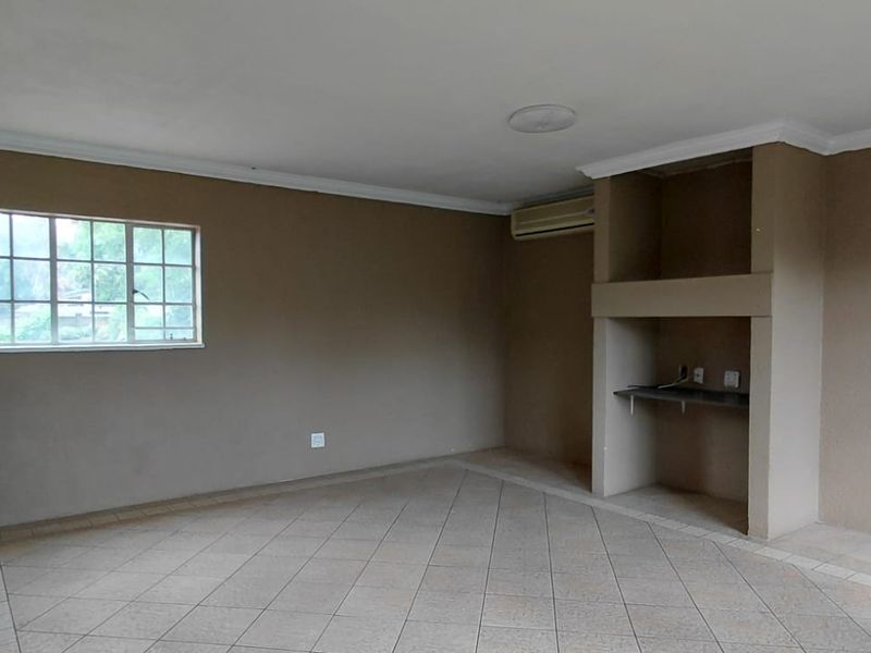 An empty living area featuring tiled flooring, a built-in shelving unit, a breakfast bar, and an air conditioning unit.