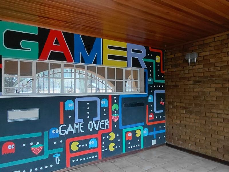 An empty living area featuring exposed brickwork, a timber ceiling, and tiled flooring, currently decorated with a prominent gaming-themed wall mural.