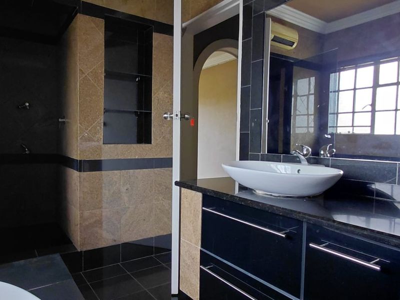 A modern bathroom featuring a double vanity with vessel sinks, dark cabinetry, and a spacious walk-in shower with tiled finishes.