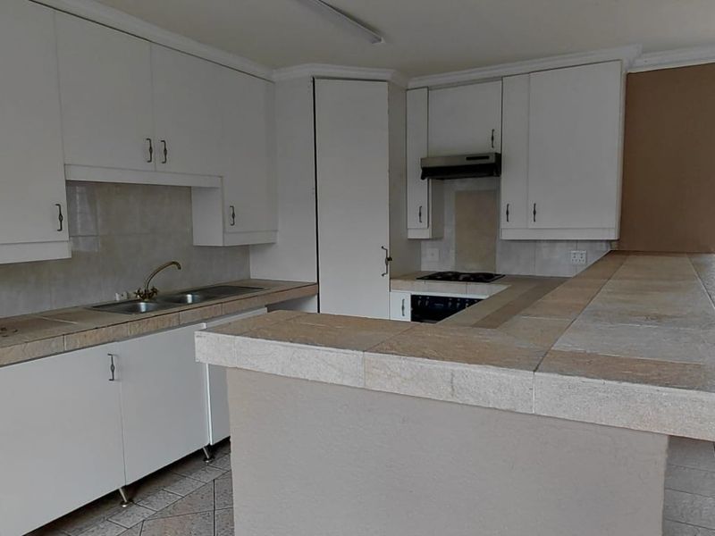 A functional kitchen featuring white built-in cabinetry, tiled countertops, a double basin sink, and integrated cooking appliances with a breakfast bar.
