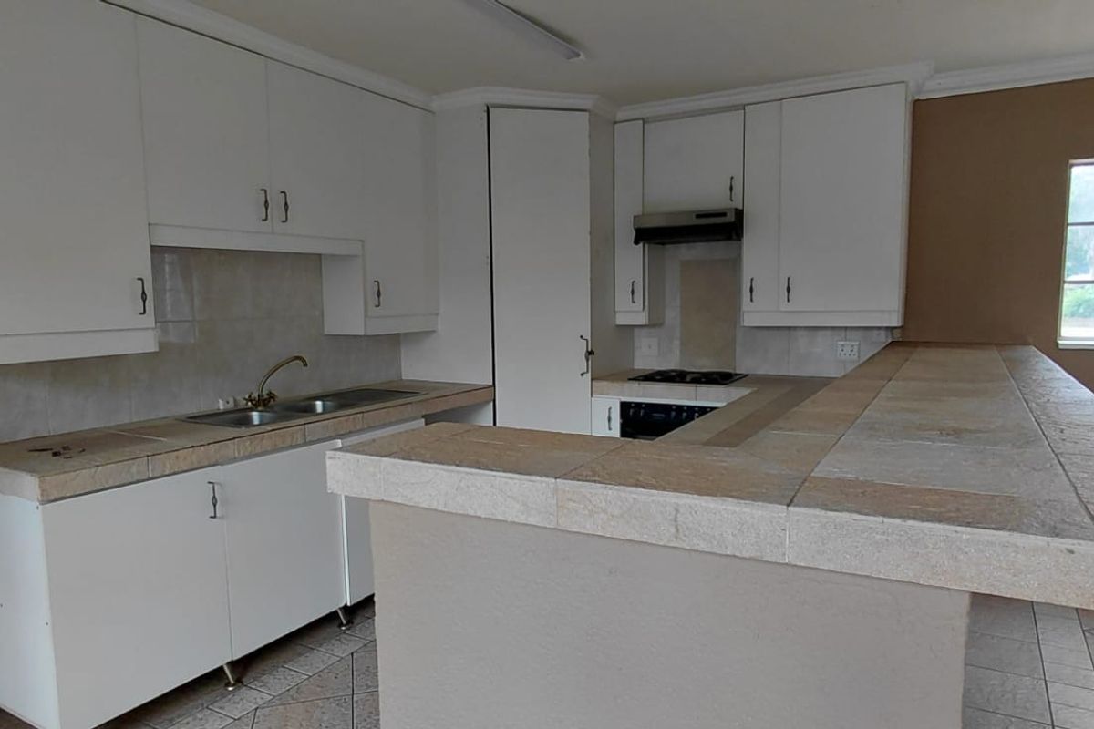 A functional kitchen featuring white built-in cabinetry, tiled countertops, a double basin sink, and integrated cooking appliances with a breakfast bar.