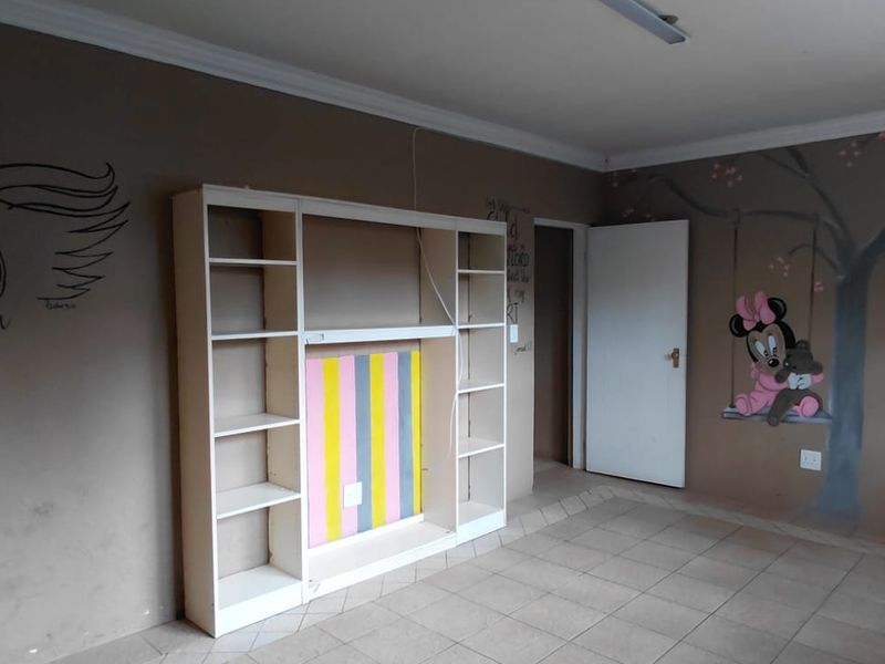 A bedroom featuring tiled flooring, a built-in shelving unit, and decorative wall murals, offering a blank canvas for potential renovation or restyling.