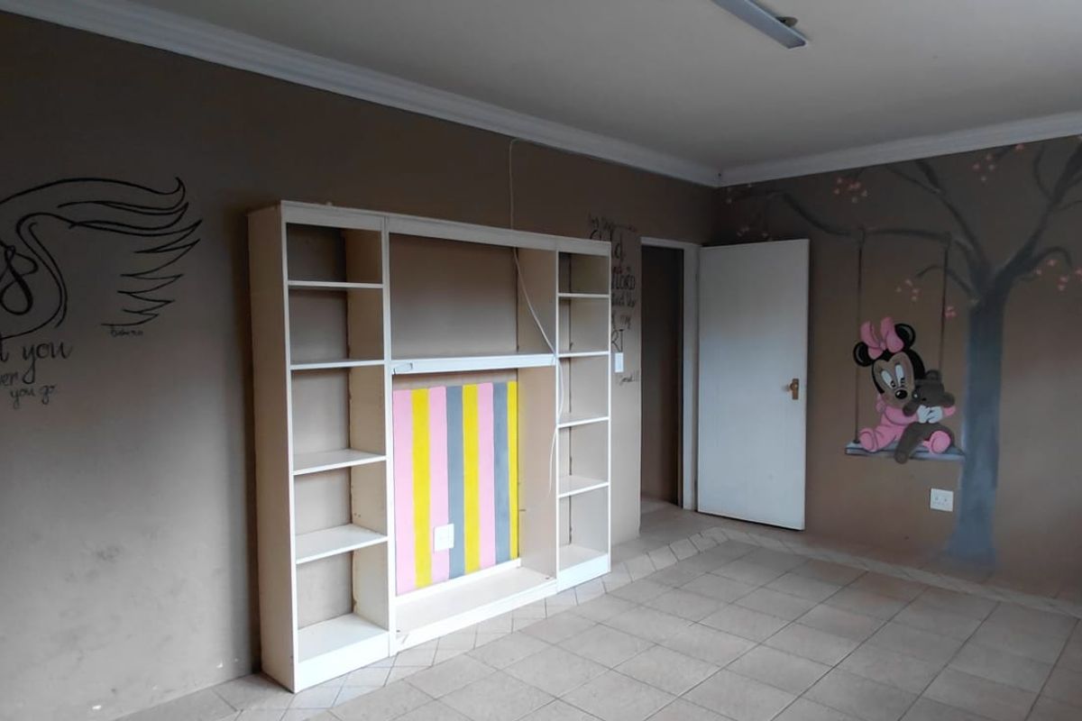 A bedroom featuring tiled flooring, a built-in shelving unit, and decorative wall murals, offering a blank canvas for potential renovation or restyling.