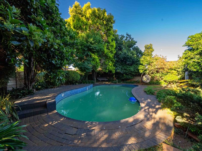 A private backyard featuring a swimming pool with a brick surround, set within a mature, landscaped garden.