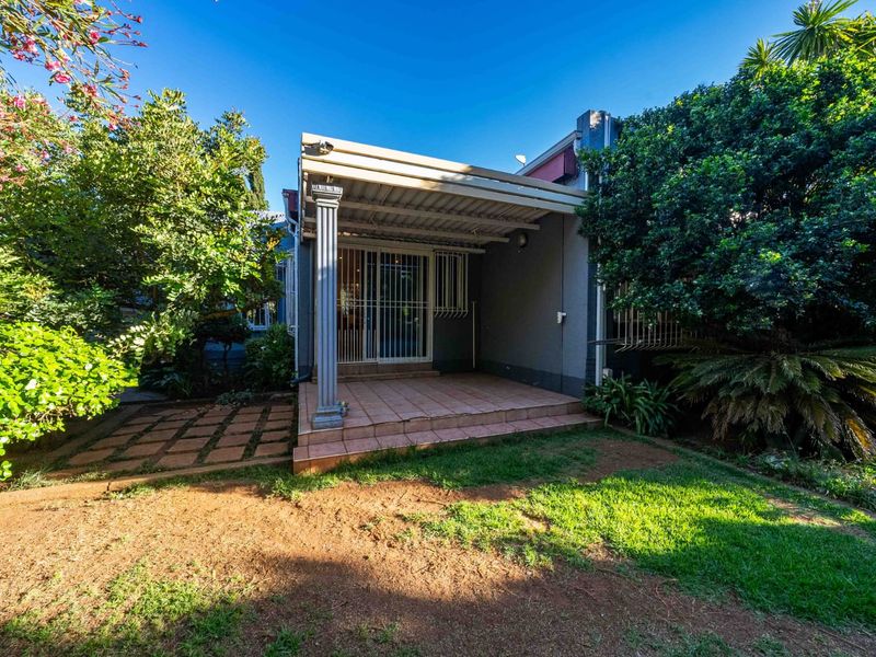 A covered patio area featuring tiled flooring and a support column, providing direct access to the garden through a sliding glass door.