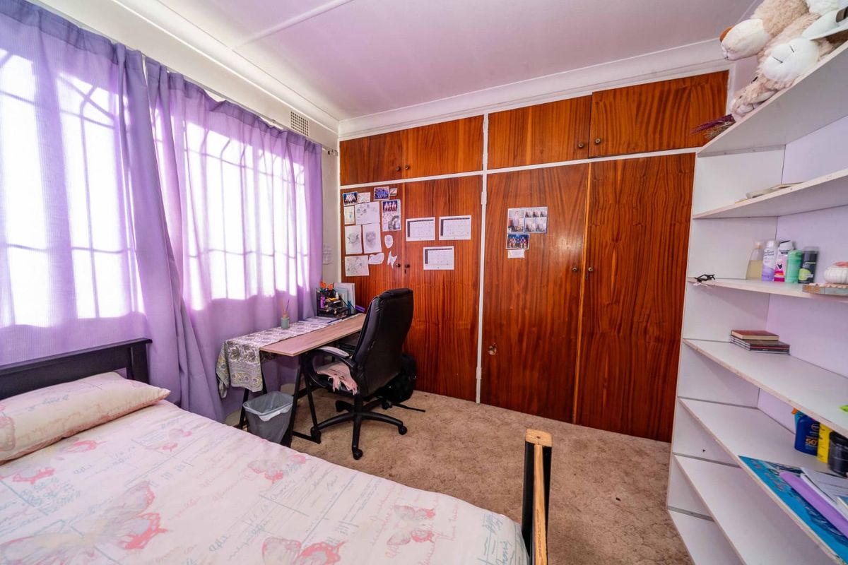 A bedroom featuring built-in wooden cupboards, carpeted flooring, and security burglar bars on the window.