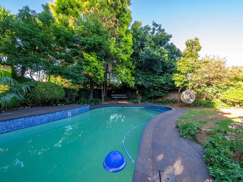 A private backyard featuring a swimming pool with mosaic tile detailing, surrounded by brick paving and established garden landscaping.