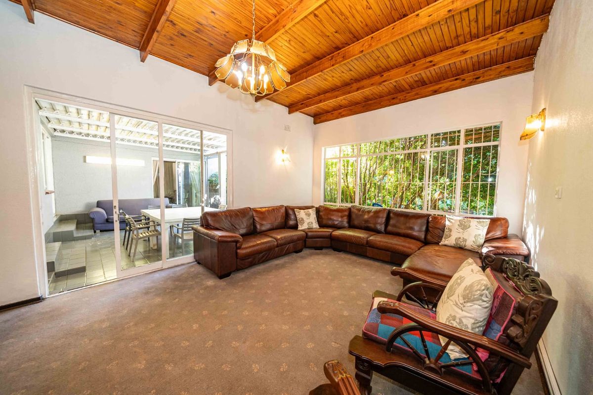 Spacious living room featuring a high exposed timber beam ceiling, large windows, and sliding glass doors leading to an adjacent patio area.