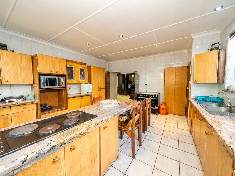 Spacious kitchen featuring extensive wooden cabinetry, granite countertops, a central island with an electric hob, and tiled flooring throughout.