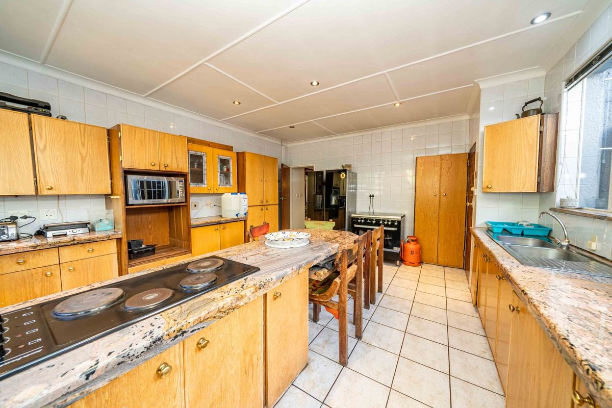 Spacious kitchen featuring extensive wooden cabinetry, granite countertops, a central island with an electric hob, and tiled flooring throughout.