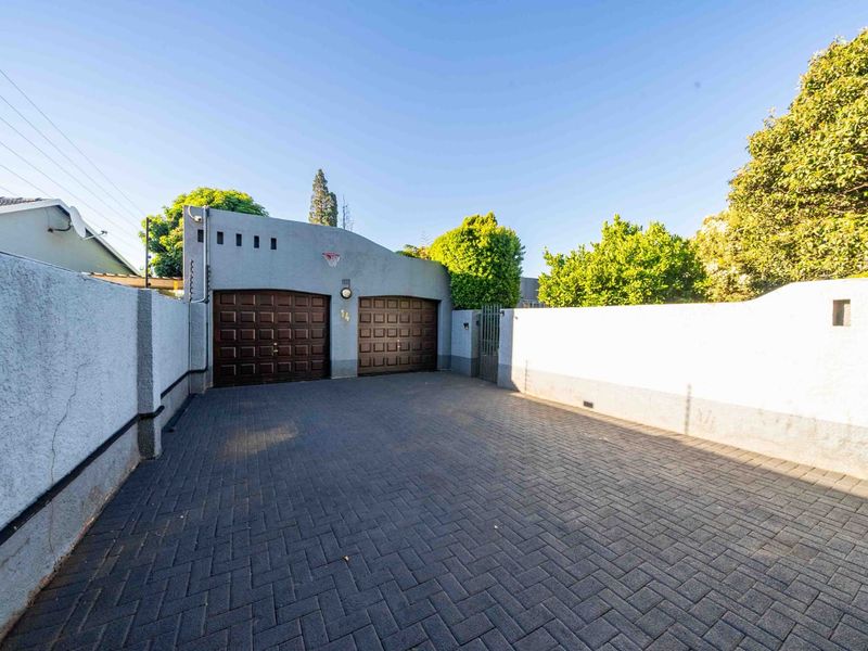 Front exterior view featuring a paved driveway leading to a double garage with a secure boundary wall and pedestrian gate.
