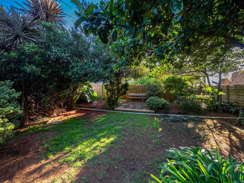 A private, well-established garden featuring mature trees, a small brick-paved seating area, and perimeter boundary walls.