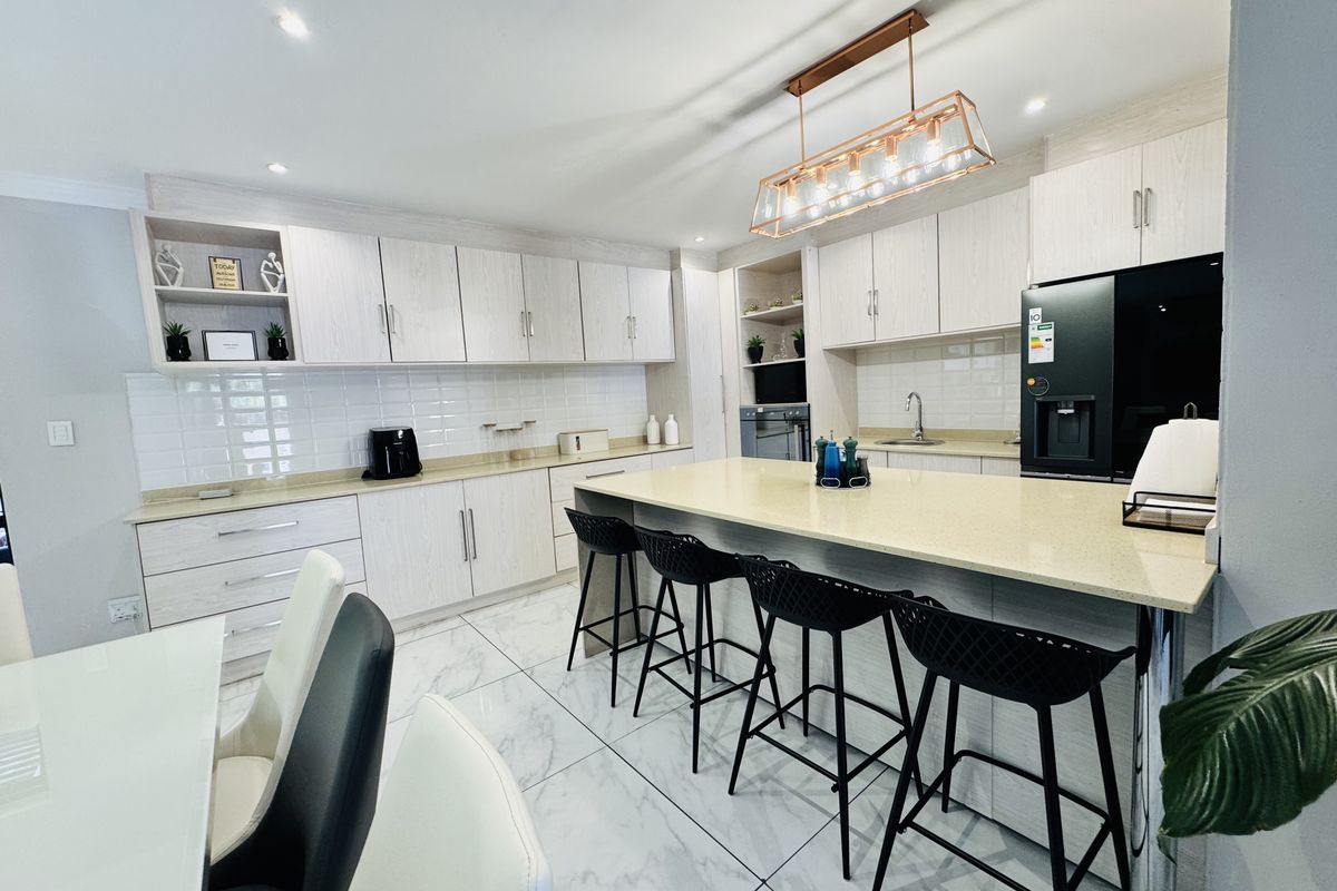 Modern kitchen featuring light wood cabinetry, quartz countertops, a central island with breakfast bar seating, and elegant marble-look porcelain floor tiles.