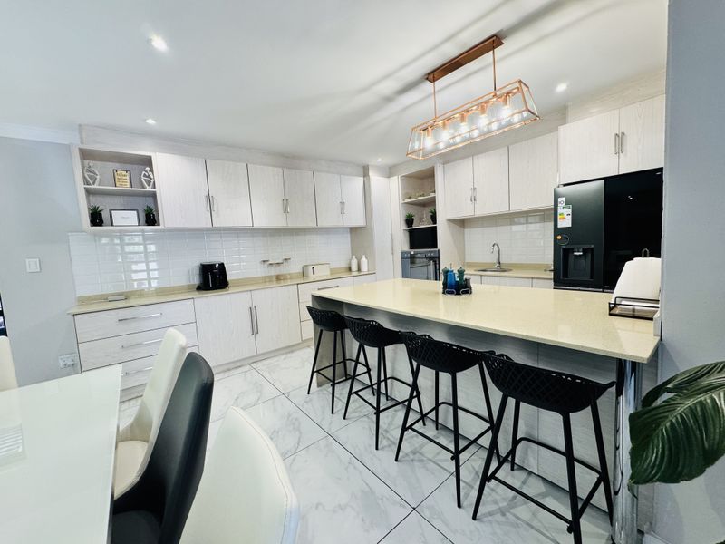 Modern kitchen featuring light wood cabinetry, quartz countertops, a central island with breakfast bar seating, and elegant marble-look porcelain floor tiles.