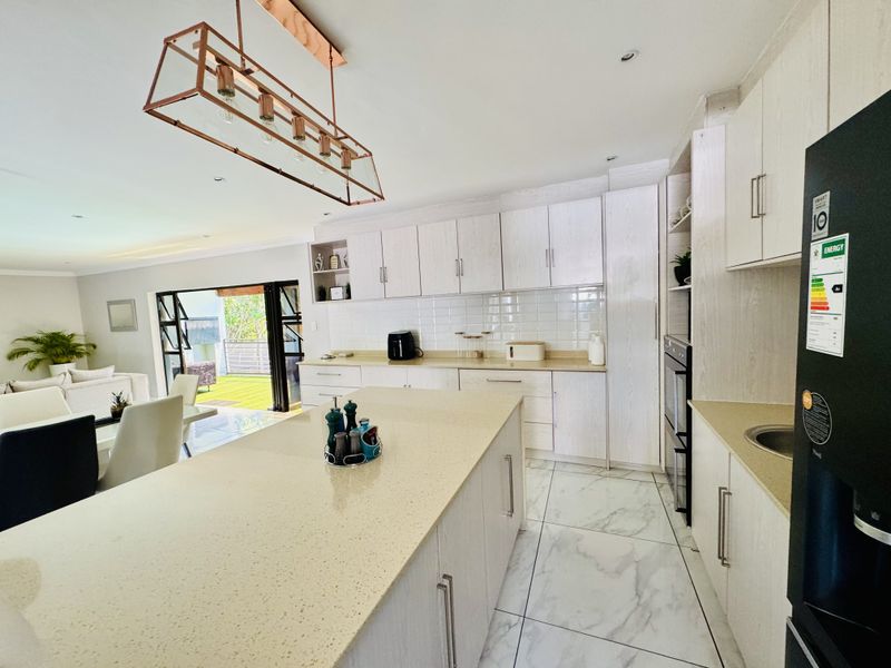Modern open-plan kitchen featuring a large island, quartz countertops, subway tile backsplash, and seamless flow to the outdoor patio area.