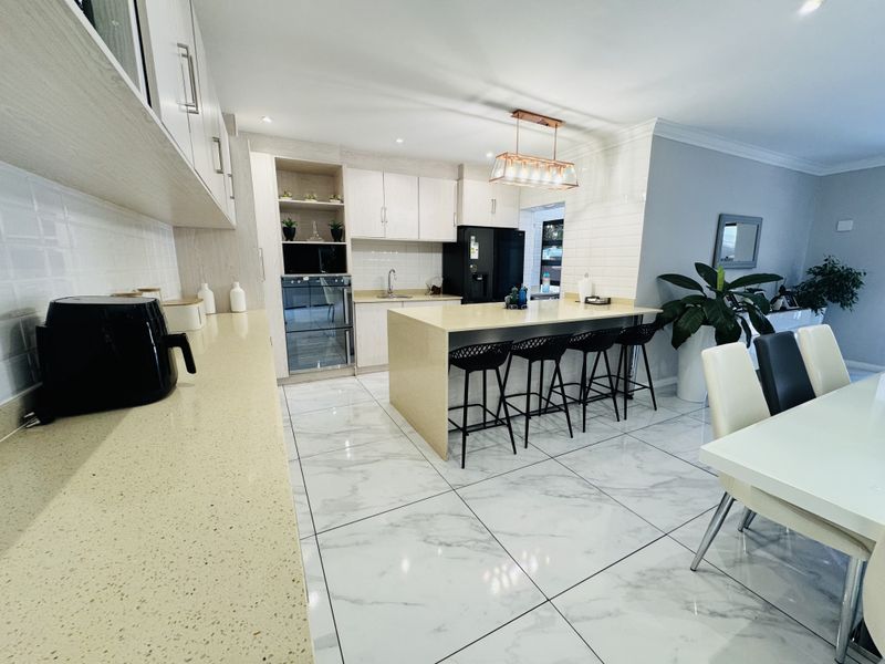 Modern open-plan kitchen featuring a central island, quartz countertops, marble-look flooring, and integrated appliances, seamlessly flowing into the dining area.