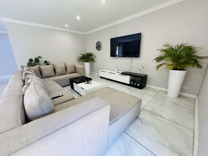 A modern, well-maintained living room featuring polished marble-look floor tiles, recessed downlighting, and coved ceiling detailing.