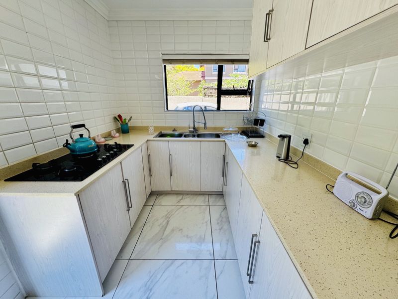 A well-maintained kitchen featuring light wood-grain cabinetry, stone countertops, a gas hob, and a double basin sink with a subway tile backsplash.