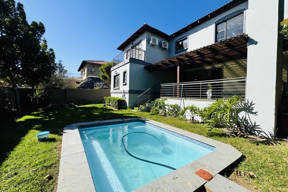 Rear exterior view featuring a swimming pool with tiled surround, a timber pergola, and a balcony overlooking the garden area.