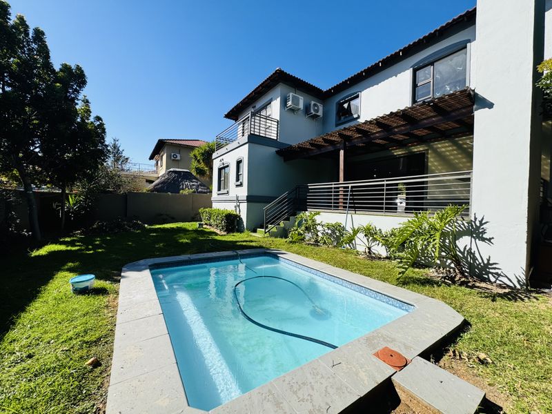 Rear exterior view featuring a swimming pool with tiled surround, a timber pergola, and a balcony overlooking the garden area.