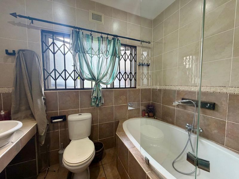 A functional bathroom featuring tiled walls and flooring, a built-in bathtub with a glass shower screen, and a standard toilet.