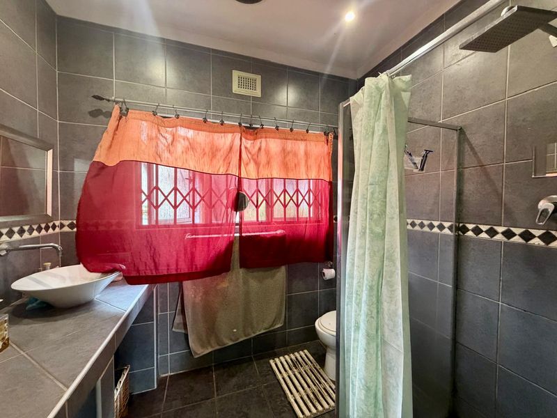 A functional bathroom featuring dark wall tiles, a vessel sink on a tiled vanity, and a walk-in shower with a rain shower head.