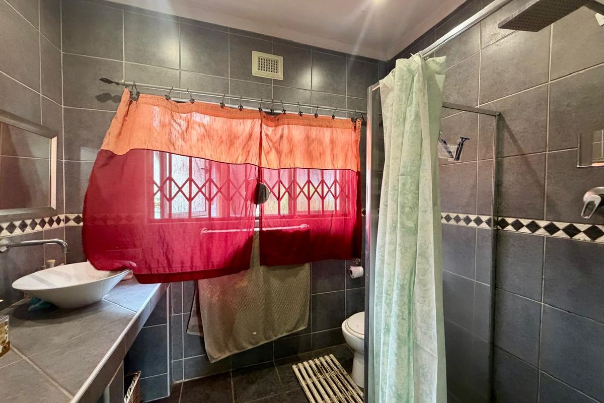 A functional bathroom featuring dark wall tiles, a vessel sink on a tiled vanity, and a walk-in shower with a rain shower head.