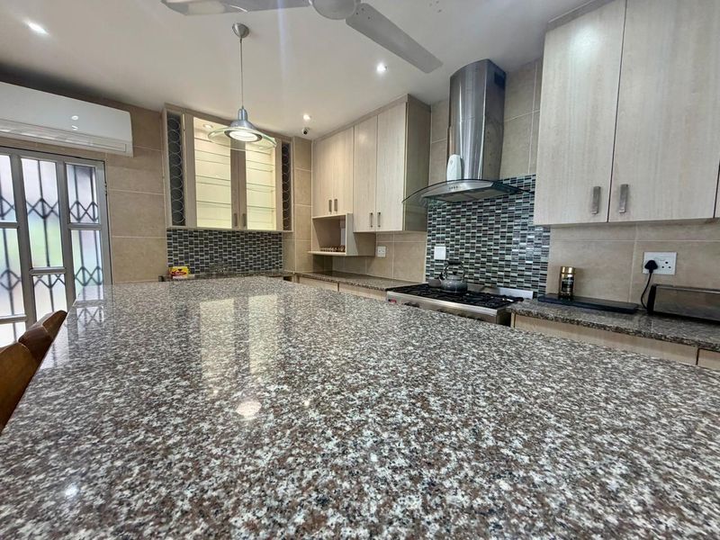 Modern kitchen featuring extensive granite countertops, built-in cabinetry, a gas hob with stainless steel extractor, and a stylish mosaic tile backsplash.