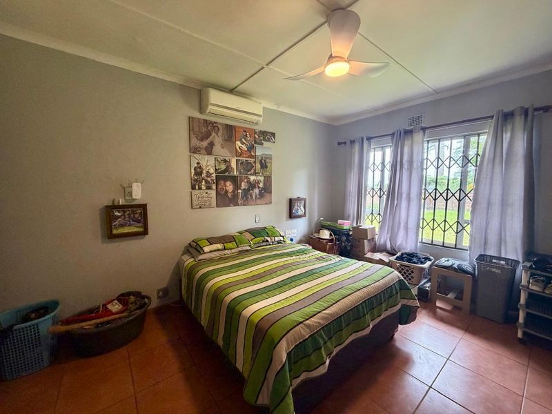 A functional bedroom featuring tiled flooring, a ceiling fan, and a wall-mounted air conditioning unit, with security bars installed on the windows.