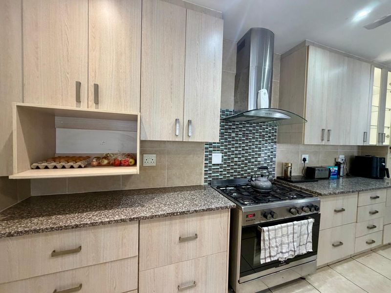 Modern kitchen featuring light wood-grain cabinetry, granite countertops, a mosaic tile backsplash, and a stainless steel gas stove with an extractor fan.