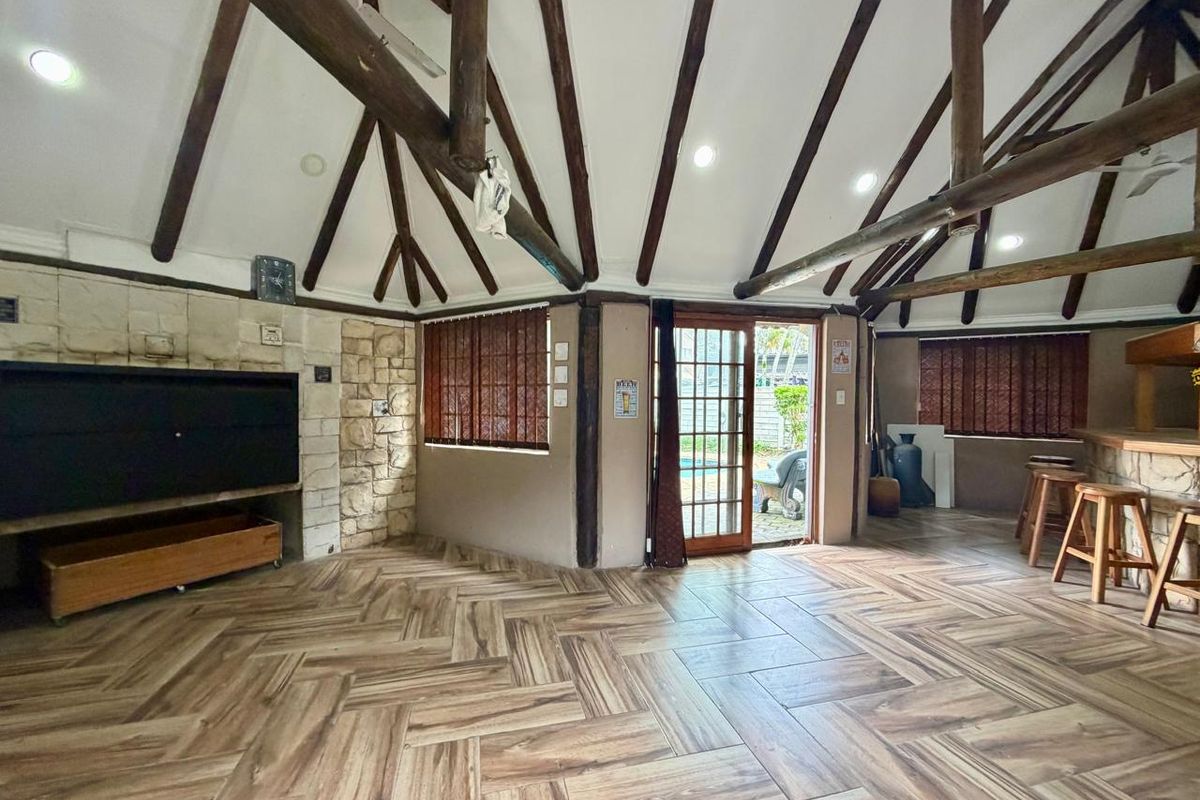 Spacious living area featuring exposed timber rafters, a stone-clad fireplace, and stylish herringbone floor tiles, with direct access to the outdoor pool area.