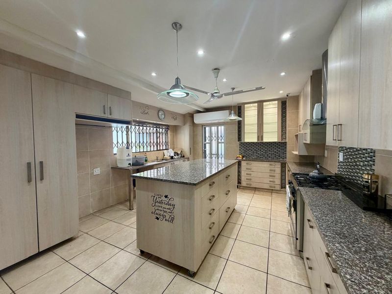 Spacious modern kitchen featuring granite countertops, a central island with storage, built-in cabinetry, gas hob, and tiled flooring throughout.