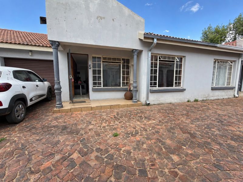 Front elevation of the apartment featuring a cobblestone driveway, tiled entrance porch, and decorative columns with a single garage.