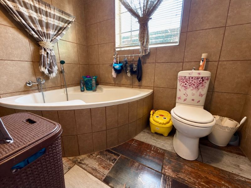 A bathroom featuring a corner bathtub, ceramic wall and floor tiling, and a standard toilet, with a window providing natural light.