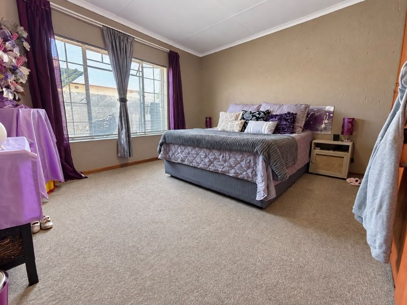 A spacious bedroom featuring neutral wall tones, carpeted flooring, and a large window that provides ample natural light.