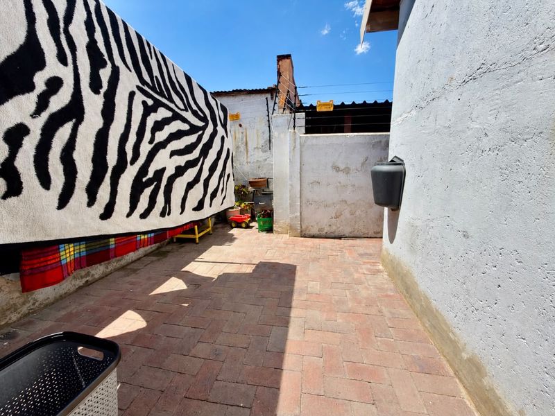 A rear exterior courtyard area featuring brick paving, perimeter walls with electric fencing, and a wall-mounted mailbox.